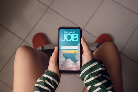 Unemployment Concept. Woman Sitting in the Toilet at Home and Using Online Job Searching Website via Mobile Phone to Finding a New Jobの写真素材