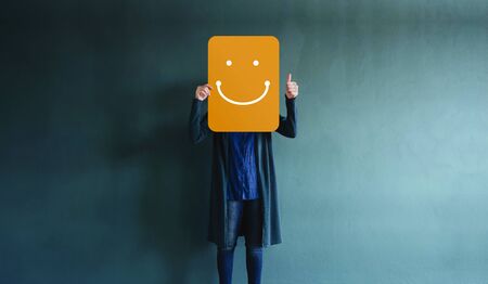 Customer Experiences or Human Emotional Concept. Woman giving Thumbs up and Showing a Happy Face Emoticon and Positive Review on Card. Client's Satisfaction Surveysの写真素材