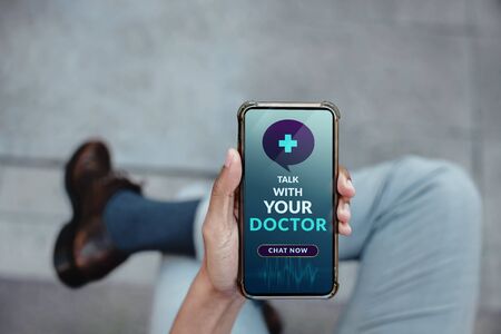 Helathy Lifestyle and Technology Concept. Modern Businessman Using Online Medicine Application via Mobile Phone to Request a Consultation from the Doctor about his Healthの写真素材