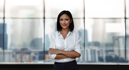 Portrait of a Smiling Mixed Races Business Woman, Crossed Arm and Look into the Camera. Blurred...