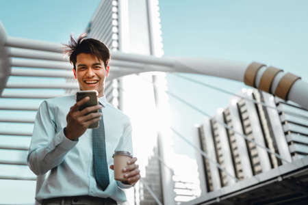 Portrait of a Smiling Young Asian Businessman Using Mobile Phone in the Cityの写真素材