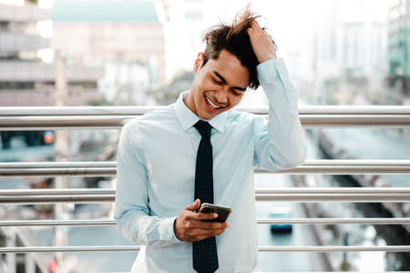 Smiling Young Asian Businessman Using Mobile Phone in the Cityの写真素材