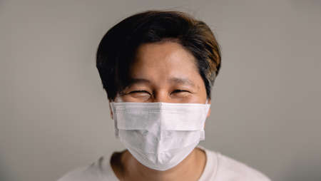 Portrait of a Happy Person, Wearing a Surgical Mask, Standing against the White Wall, Smiling inside a Maskの写真素材