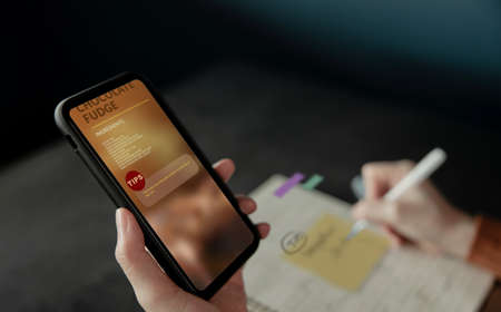 E-Learning at Home Concept. Woman Note a Tips for Cooking Chocolate Fudge via the Internet on Mobile...