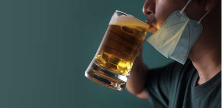 Drinking Beer in Covid-19 Situation Concept. Person wearing a Surgical Mask on Chin while Drinking a...