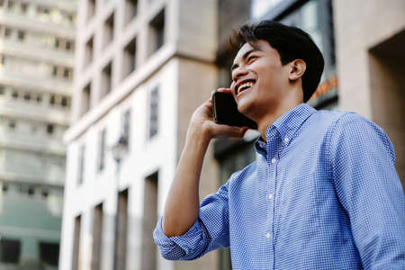 Smiling Young Asian Businessman Using Mobile Phone in the Cityの写真素材