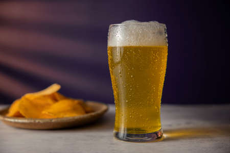 Glass of Beer and plate with Potato Chips on Table. Drinking Beer at Home or Cafeの写真素材