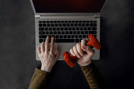 Work Life Balance Concept. Young Woman holding a Dumbbell to Exercising Hand and Arm while Working on Computer Laptop. Mental Health Care. Top Viewの写真素材