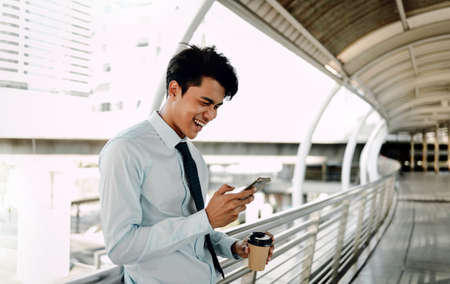Portrait of a Smiling Young Asian Businessman Using Mobile Phone in the Cityの写真素材