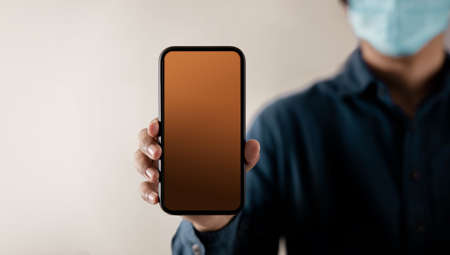 Mobile Phone Mockup Image. Display Screen is Blank. Person with a Surgical Mask on Face Holding a...