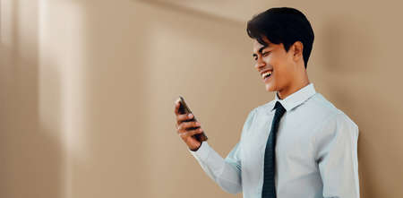 Portrait of a Smiling Young Asian Businessman Using Mobile Phone by the Wall