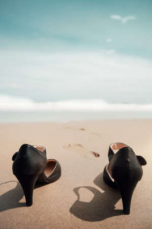 Work Life Balance Concept. Business Woman take off her Working Shoes and leave it on the Sand Beach for Walk into the Sea on Sunny Day. Quit a Job, Office Outing or Summer Vacation. Vertical and Low angle Viewの写真素材