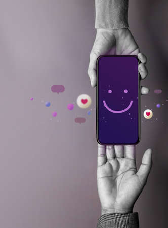 Customer Experience Concept. Happy Client giving a Smiling Emoticon via Mobile Phone to Brand. Feedback on Smartphone. Positive Review. Online Satisfaction Surveyの写真素材