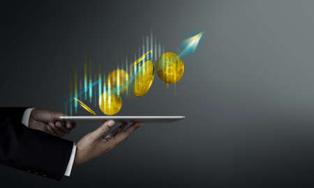 Money Investment on Crypto Currency Coin Concept. Businessman Holding Digital Tablet with Golden Bitcoin Floating by Up Arrow and Stock Market Graphの写真素材