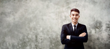 Smiling Young Businessman Standing by the Loft Concrete Wall. Crossed Arms and Looking at Camera. more copy space with Wide sizeの写真素材