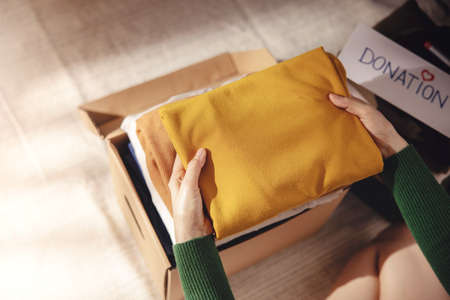 Clothes Donation Concept. Box of Cloth with Donate label. Woman Preparing Used Old Garment at Home. Top Viewの写真素材