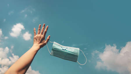 Hope, Positive Mind for Coronavirus Concept. Hand Raised Up a Smiling Medical Mask into the Blue Sky. Gesture means Goodbye. Deep Breathing for Fresh Airの写真素材