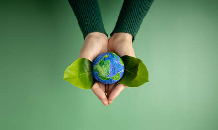 World Earth Day Concept. Green Energy, ESG, Renewable and Sustainable Resources. Environmental and Ecology Care. Hands of Person  Embracing Green Leaf and Craft Globeの写真素材