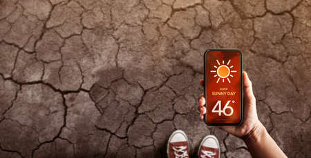 Water Crisis Concept. Environmental Impact. Global Issues in Agricultural. Standing on Cracked Soil with High Temperature Weather on Mobile Phone. Desertification, Pollution, Energy and Climate Changeの写真素材