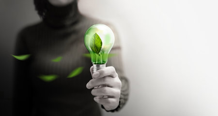 Green Energy, Renewable and Sustainable Resources in Environmental Concept. Woman holding a Green Leaf with Light Bulbの写真素材