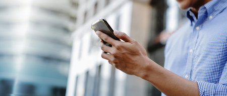 A man using a smartphone in an urban environment, representing mobile communication, digital lifestyle, and business on the goの写真素材