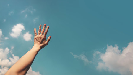 Hand reaching toward the bright blue sky, symbolizing freedom, hope, positivity, and human aspiration to reach higher goalsの写真素材