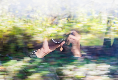 Blur traveler photographer  hold camera reflect on high speed train window while running with nature forest background.の写真素材