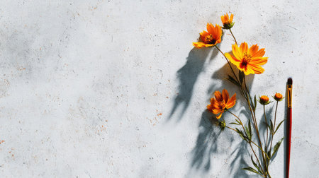 A vibrant arrangement of bright orange flowers beside a paintbrush on a gray textured background, evoking creativity and artistic inspiration in a serene setting.の素材