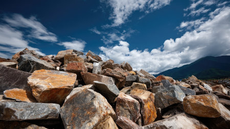 A stunning view of a pile of multicolored rocks against a vibrant blue sky with fluffy white clouds. This natural scene captures the beauty of the outdoors and geological diversity.の素材