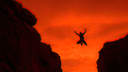 A lone figure leaps into the air against a stunning orange sunset backdrop, capturing the essence of freedom and adventure in a dramatic cliff landscape.の素材