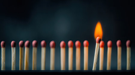A single match ignites amidst a row of unlit matches, creating a mesmerizing display of light and shadow, symbolizing individuality and energy against a dark backdrop.の素材