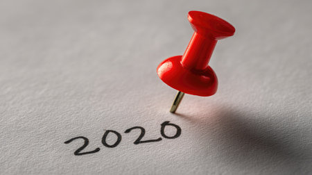 A vivid red thumbtack sits on a sheet of paper, drawing attention to the year 2020. This image symbolizes planning, reminders, and important events that define a year.の素材