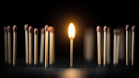 A striking image of a single lit match surrounded by unlit matchsticks. The bright flame stands out against the dark background, symbolizing hope and inspiration.の素材