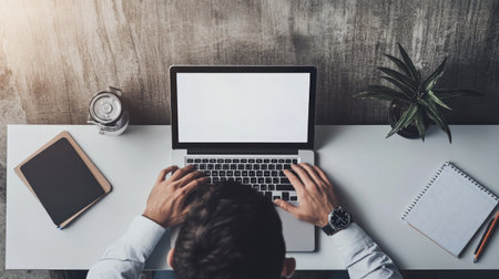 A focused individual types on a laptop in a minimalist office setting. The scene captures technology, organization, and productivity with elements like coffee and greenery.の素材