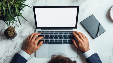 Aerial view of a person typing on a laptop surrounded by a minimalist workspace featuring a green plant, showcasing productivity and modern office aesthetics.の素材