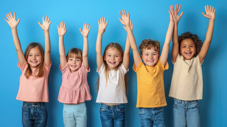 Five cheerful children raise their hands in joyful celebration against a bright blue background, capturing the essence of happiness and togetherness in childhood.の素材