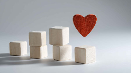 A creative composition featuring wooden blocks and a red heart on a gray background. This image symbolizes love and connection through minimalistic design.の素材