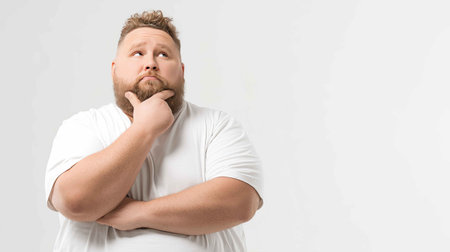 A thoughtful man in a white shirt poses in a studio setting, showing a contemplative expression while he considers an idea, conveying emotion and reflection.の素材