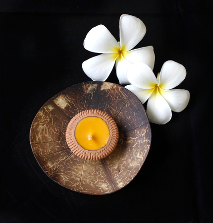 The coconut shell candle holder with the plumeria decoration on the black backgroundの写真素材
