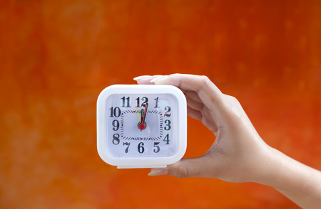 Hand holding clock with space on orange wallの写真素材