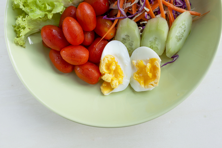Fresh vegetable salad with egg in green plate on wood backgroundの写真素材