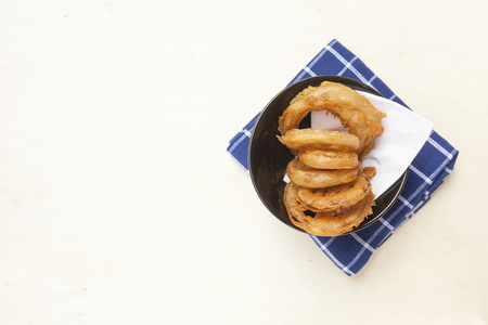 Golden onion ring in black bowl on blue napkin with space on white wooden tableの写真素材