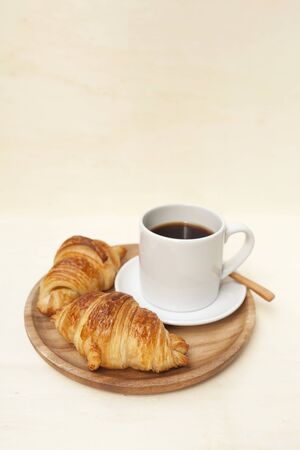 Golden brown croissant and black coffee on wooden plate with space on backgroundの写真素材