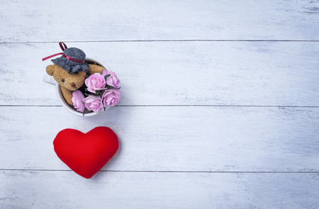 Teddy bear with pink flower with red heart on white wood backgroundの写真素材