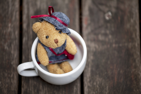 Little teddy bear in white cup with dark wood backgroundの写真素材