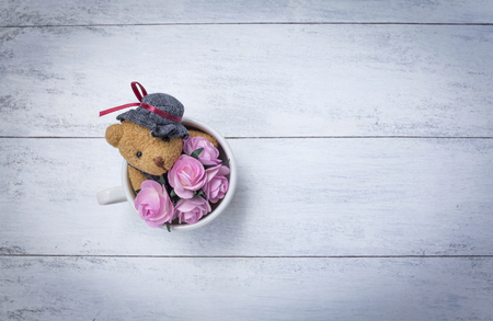 Little teddy bear holding pink roses flower in coffee cup with space on white wood tableの写真素材