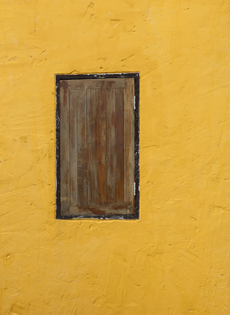 Yellow cement wall with old wooden windowの写真素材
