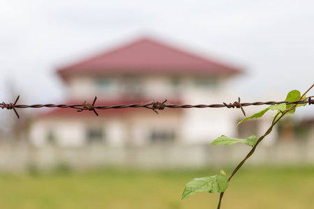 Rusty Barbed wire fence with blur big house on backgroundの写真素材