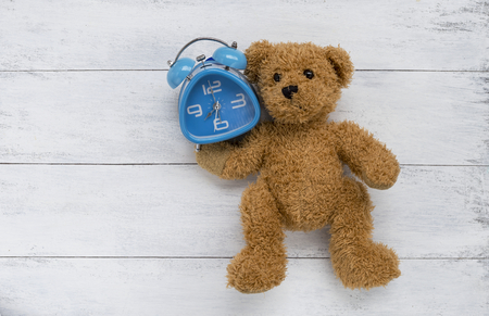 Brown teddy bear carry blue clock with space on wooden floorの写真素材