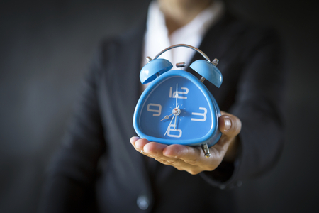 Business girl holding blue clock with space on black backgroundの写真素材